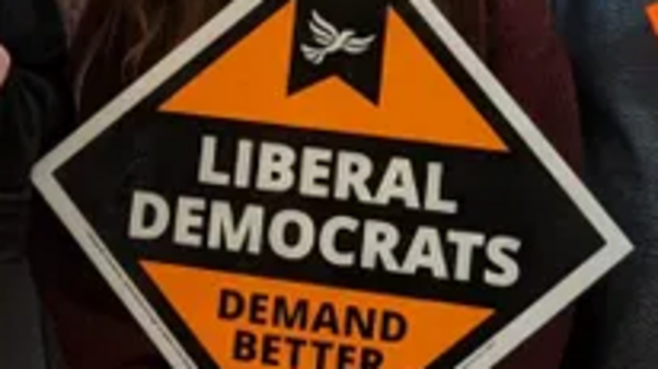 Lib Dem diamond with "Demand Better" written on it